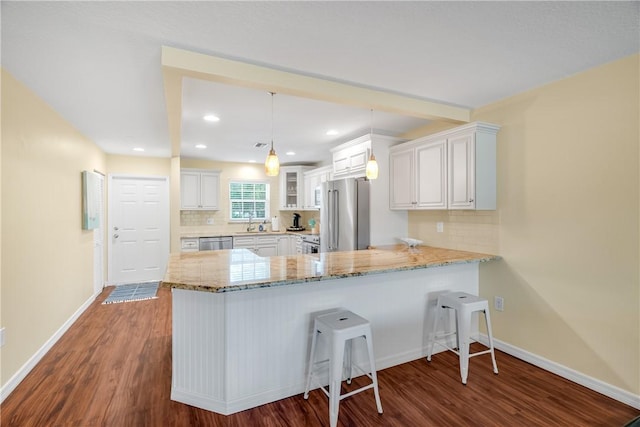 kitchen with white cabinetry, hanging light fixtures, appliances with stainless steel finishes, kitchen peninsula, and hardwood / wood-style flooring