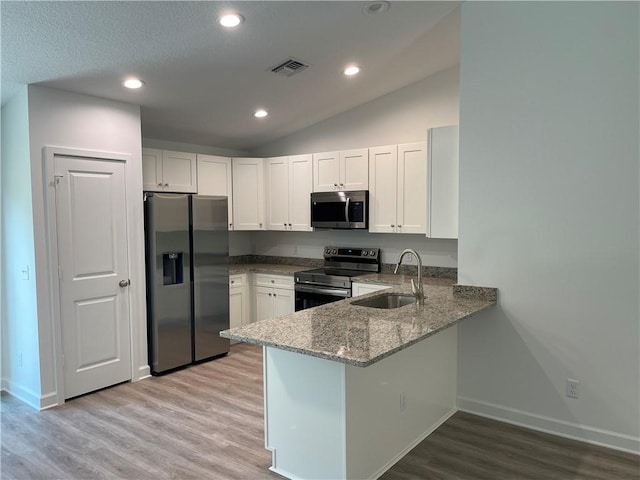 kitchen with vaulted ceiling, white cabinetry, sink, light stone counters, and stainless steel appliances