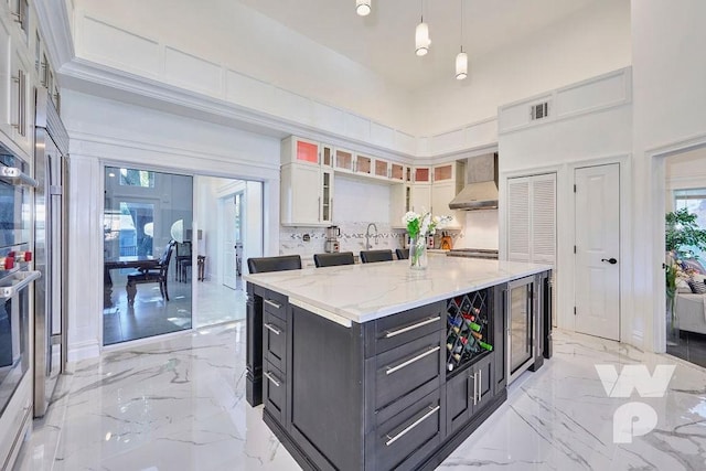 kitchen with marble finish floor, white cabinets, wall chimney range hood, and a high ceiling