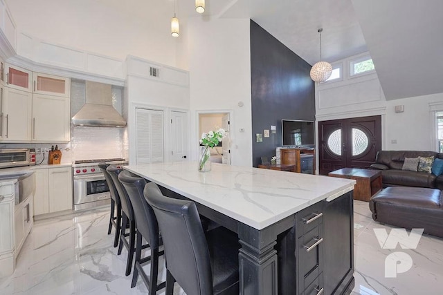 kitchen with high end stainless steel range oven, wall chimney exhaust hood, decorative light fixtures, and white cabinets