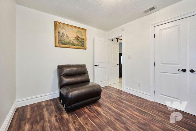 living area featuring visible vents, a textured ceiling, baseboards, and wood finished floors