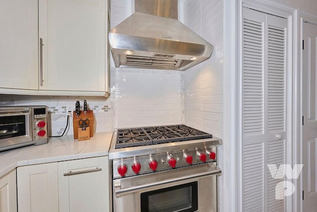 kitchen with wall chimney range hood, premium stove, backsplash, and white cabinets