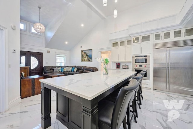 kitchen with a kitchen island, appliances with stainless steel finishes, pendant lighting, white cabinetry, and light stone counters