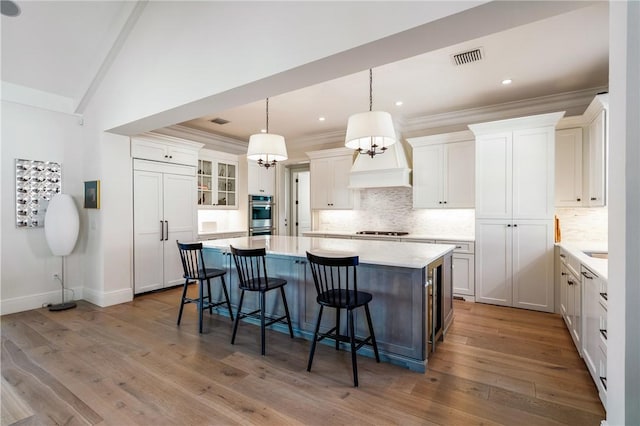 kitchen featuring white cabinetry, wood-type flooring, a center island, appliances with stainless steel finishes, and pendant lighting