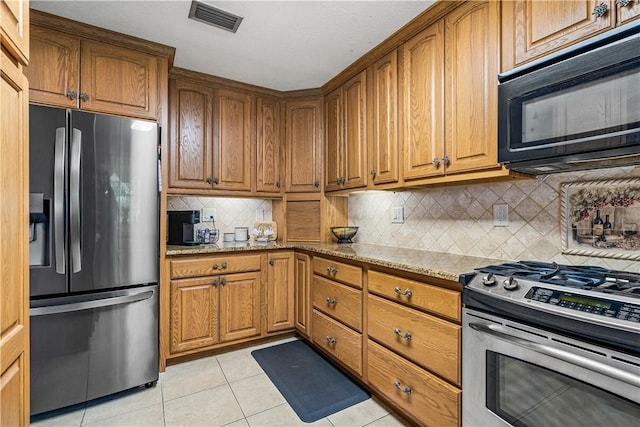 5845 23rd St, Vero Beach, FL 32966 - kitchen featuring appliances with stainless steel finishes, light stone counters, light tile patterned flooring, and brown cabinets