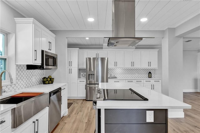 kitchen with island exhaust hood, stainless steel appliances, light hardwood / wood-style flooring, white cabinets, and a kitchen island