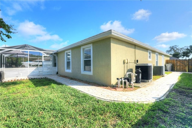 view of property exterior with central AC unit, glass enclosure, and a lawn