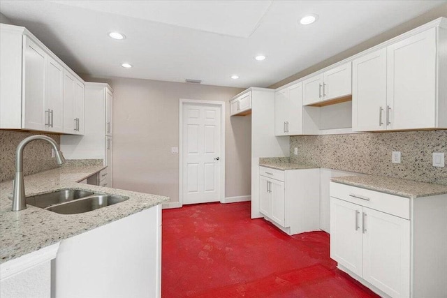 kitchen with decorative backsplash, light stone countertops, dark carpet, sink, and white cabinetry