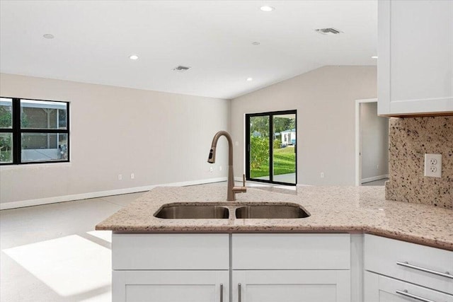 kitchen with light stone countertops, tasteful backsplash, vaulted ceiling, sink, and white cabinets