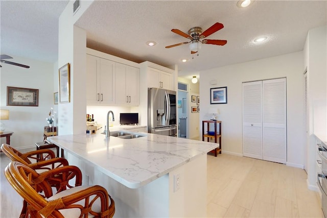 kitchen with a breakfast bar area, smart refrigerator, white cabinets, ceiling fan, and a peninsula