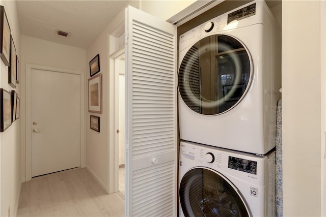 laundry area with stacked washing maching and dryer, light wood-type flooring, and a textured ceiling