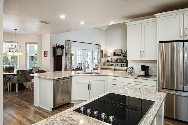 kitchen with appliances with stainless steel finishes, white cabinetry, tasteful backsplash, sink, and light stone counters