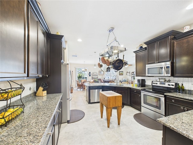 kitchen featuring light stone counters, stainless steel appliances, dark brown cabinets, and decorative backsplash