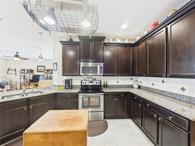 kitchen featuring dark brown cabinetry, light stone countertops, stainless steel appliances, backsplash, and a sink