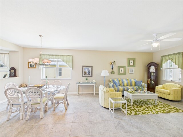 living area featuring tile patterned flooring, ceiling fan with notable chandelier, and baseboards