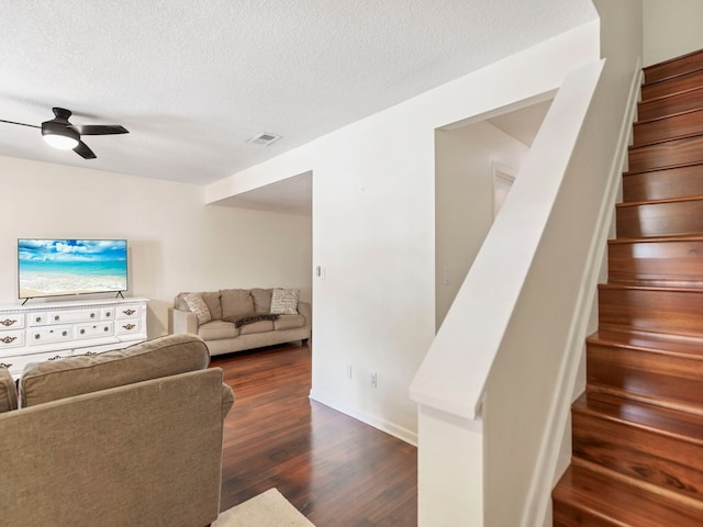 living room with a textured ceiling, dark wood-type flooring, and ceiling fan