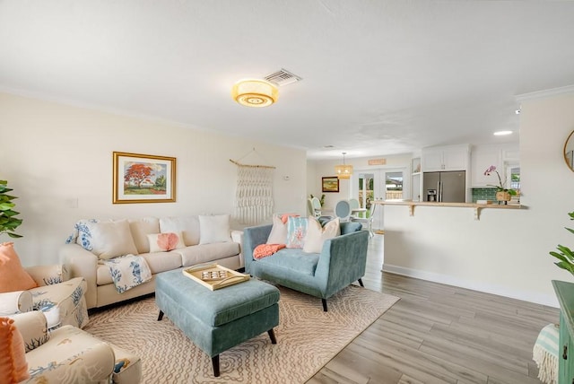 living area with light wood-style floors, baseboards, visible vents, and crown molding