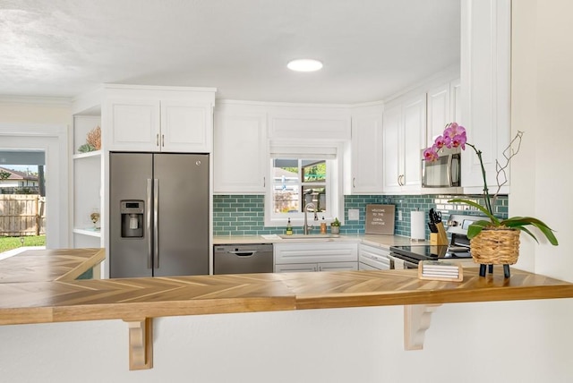 kitchen with a sink, wood counters, white cabinets, appliances with stainless steel finishes, and tasteful backsplash