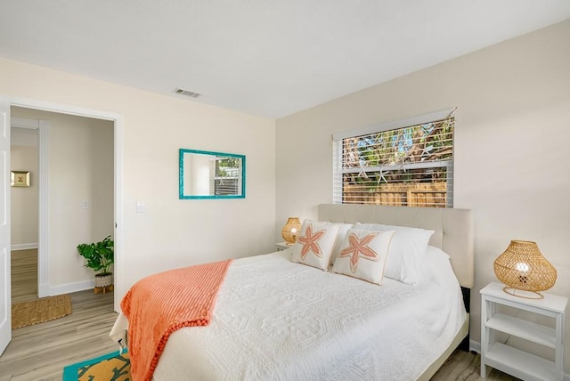 bedroom with baseboards, visible vents, and wood finished floors