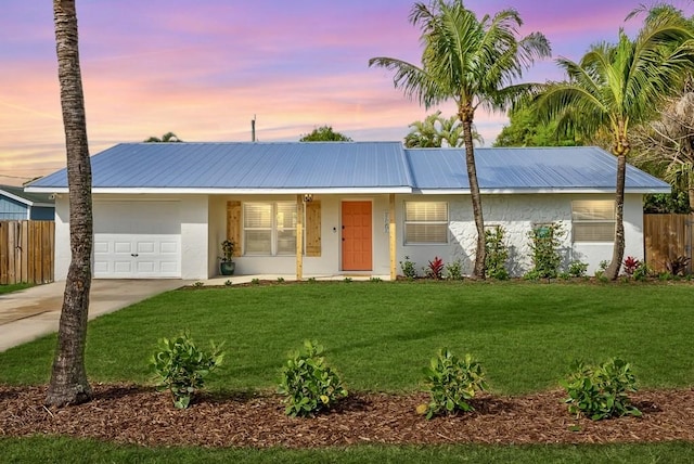 view of front of house featuring metal roof, a garage, fence, a yard, and stucco siding