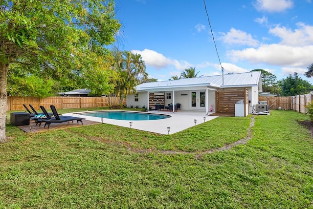 rear view of property with metal roof, a patio, a fenced backyard, french doors, and a lawn