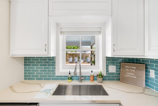 kitchen featuring light stone countertops, white cabinets, and a sink