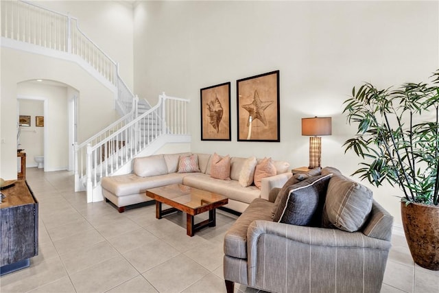 living area featuring arched walkways, a high ceiling, stairs, and light tile patterned floors
