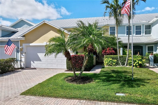 view of front facade featuring a front lawn, stucco siding, metal roof, decorative driveway, and a garage