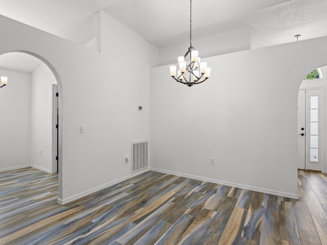 spare room featuring a textured ceiling, an inviting chandelier, and dark wood-type flooring