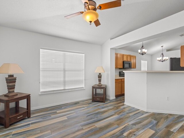 unfurnished living room with ceiling fan with notable chandelier, dark wood-type flooring, and lofted ceiling