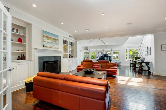 living room featuring crown molding, a tiled fireplace, dark wood-type flooring, and built in features