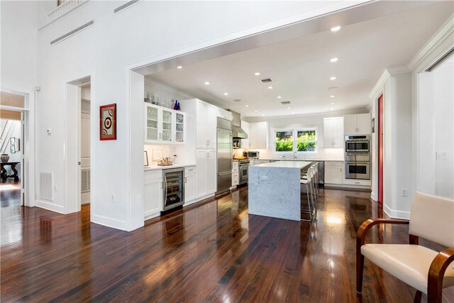 kitchen with a kitchen island, dark hardwood / wood-style floors, white cabinetry, beverage cooler, and stainless steel appliances