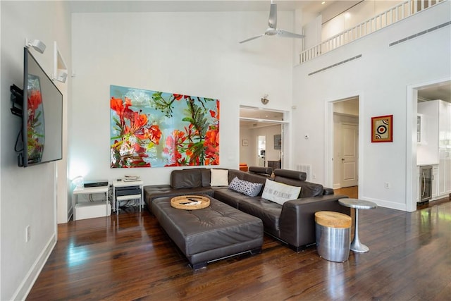 living room featuring dark wood-type flooring, ceiling fan, and a towering ceiling