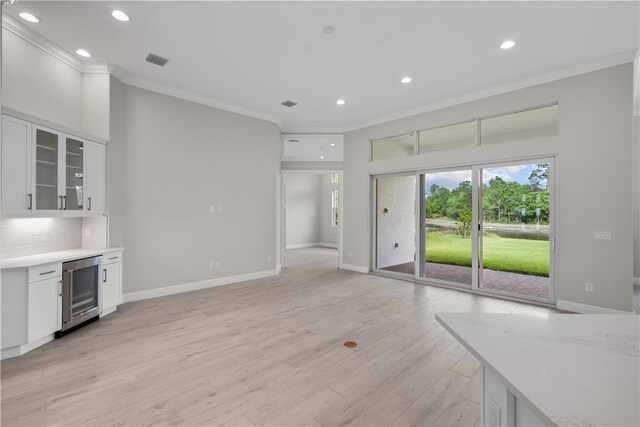 kitchen featuring beverage cooler, white cabinets, ornamental molding, light stone countertops, and light hardwood / wood-style flooring