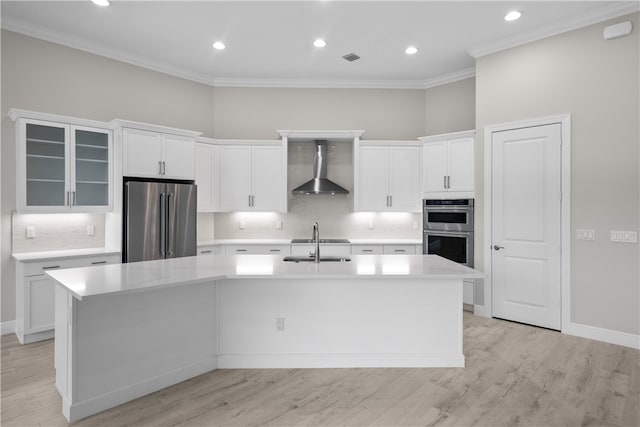 kitchen featuring stainless steel appliances, an island with sink, white cabinets, wall chimney range hood, and light wood-type flooring