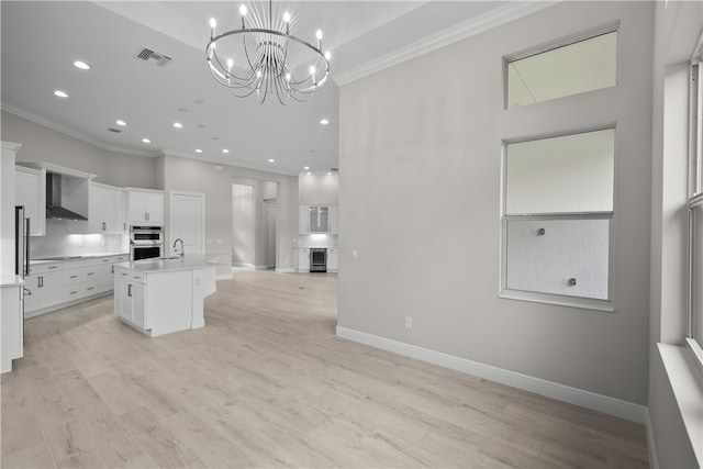 kitchen featuring double oven, white cabinetry, light wood-type flooring, an island with sink, and wall chimney exhaust hood