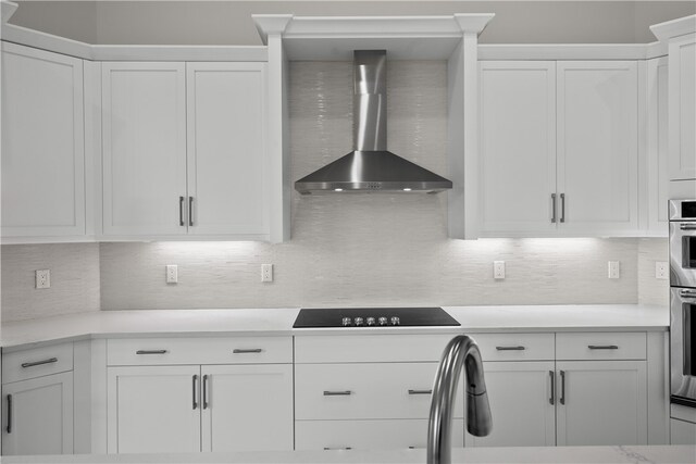 kitchen with black electric cooktop, wall chimney exhaust hood, backsplash, white cabinets, and stainless steel oven