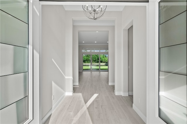 hall with a notable chandelier, light wood-type flooring, and ornamental molding