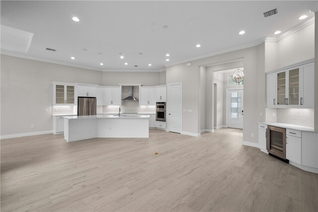 kitchen featuring stainless steel appliances, light hardwood / wood-style floors, beverage cooler, white cabinets, and wall chimney exhaust hood