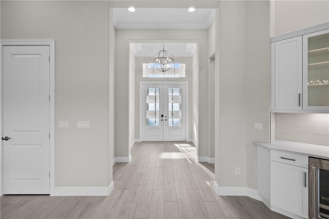 foyer featuring a chandelier, beverage cooler, light wood-type flooring, and crown molding