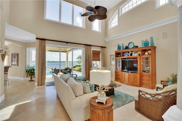 living room with a towering ceiling, ceiling fan, crown molding, and light tile patterned floors