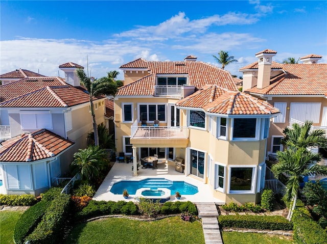 rear view of house with a balcony, an in ground hot tub, and a patio area