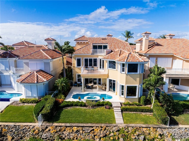 rear view of house with a pool with hot tub, a lawn, and a balcony