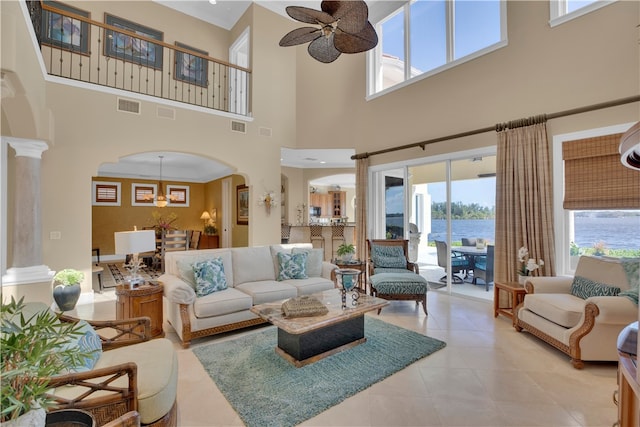 living room featuring a towering ceiling, a water view, ceiling fan, and decorative columns