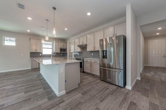 kitchen featuring decorative light fixtures, dark wood-type flooring, stainless steel appliances, sink, and a kitchen island with sink