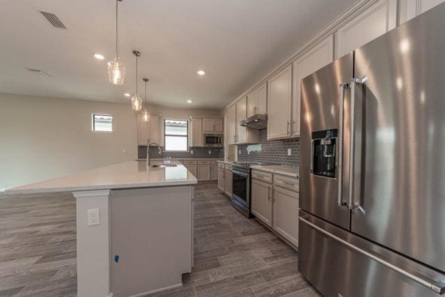 kitchen featuring hanging light fixtures, a kitchen island with sink, sink, dark hardwood / wood-style flooring, and stainless steel appliances