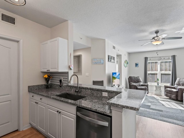 kitchen with a peninsula, a sink, open floor plan, dishwasher, and light wood-type flooring