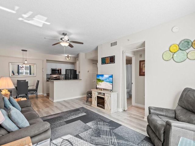 living area with light wood-type flooring, visible vents, a textured ceiling, and ceiling fan