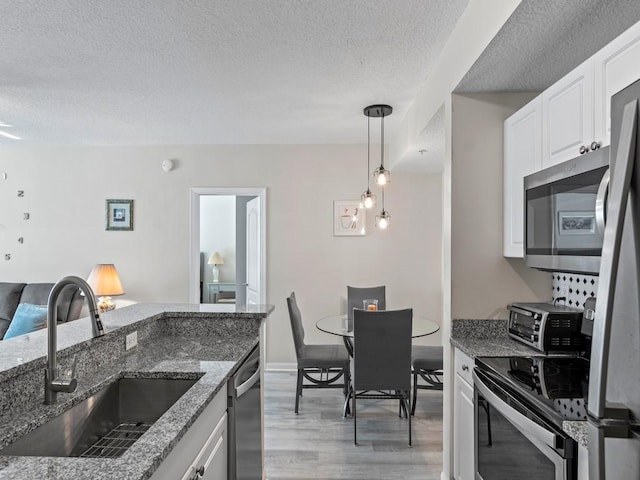 kitchen featuring stone countertops, a sink, light wood-style floors, appliances with stainless steel finishes, and white cabinetry