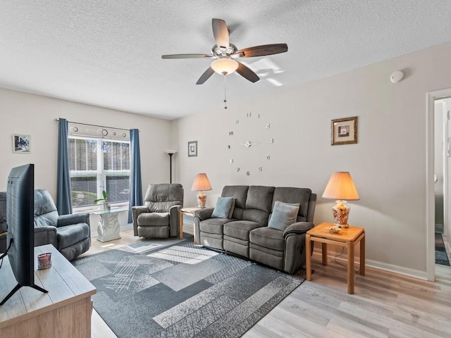 living room featuring a ceiling fan, light wood-style floors, baseboards, and a textured ceiling